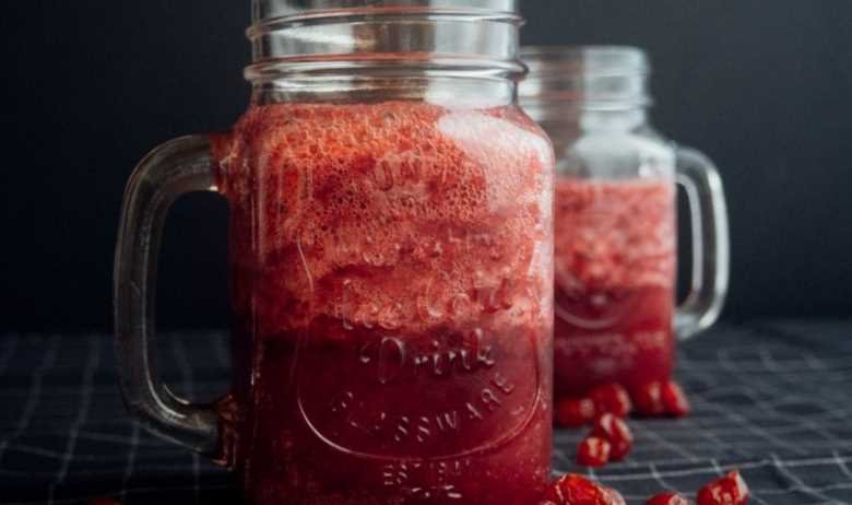 A pair of mason jars filled with fresh cranberry juice, with cranberries resting on a countertop