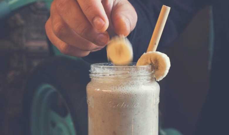 A man placing two slices of banana onto the rim of a mason jar filled with a protein shake