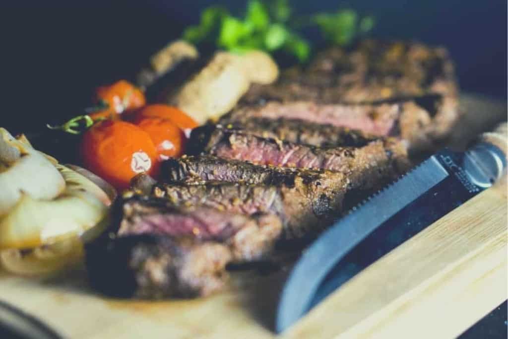 Sliced steak on a wooden cutting board with a collection of sides