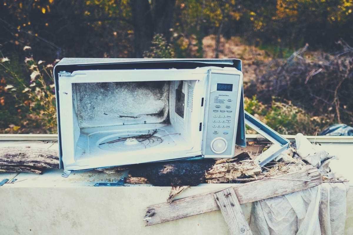 A partially destroyed microwave sitting outside on a broken sidetable