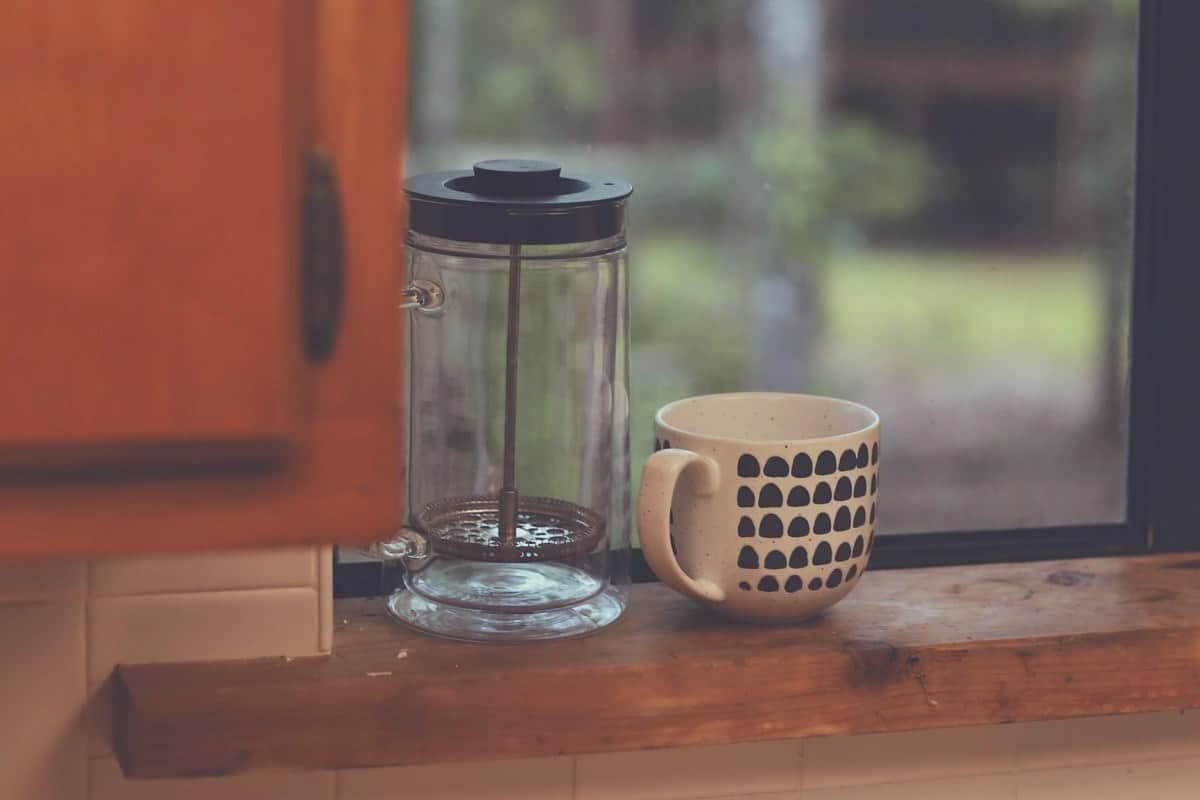 A French Press and a cup sitting on a windowsill