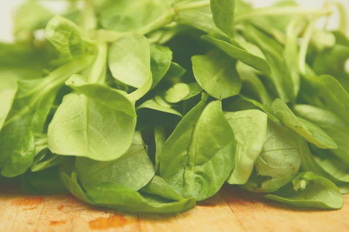 A large pile of spinach on a wooden cutting board