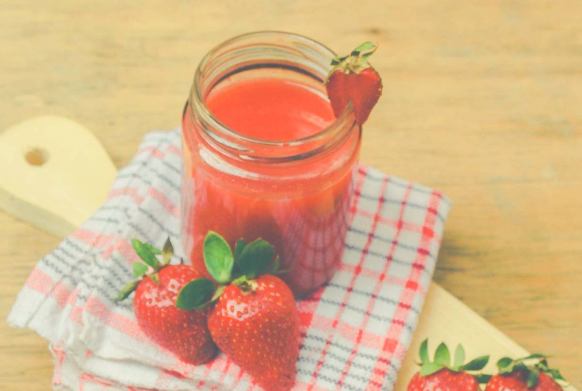 A strawberry smoothie on a cutting board with fresh strawberries around it