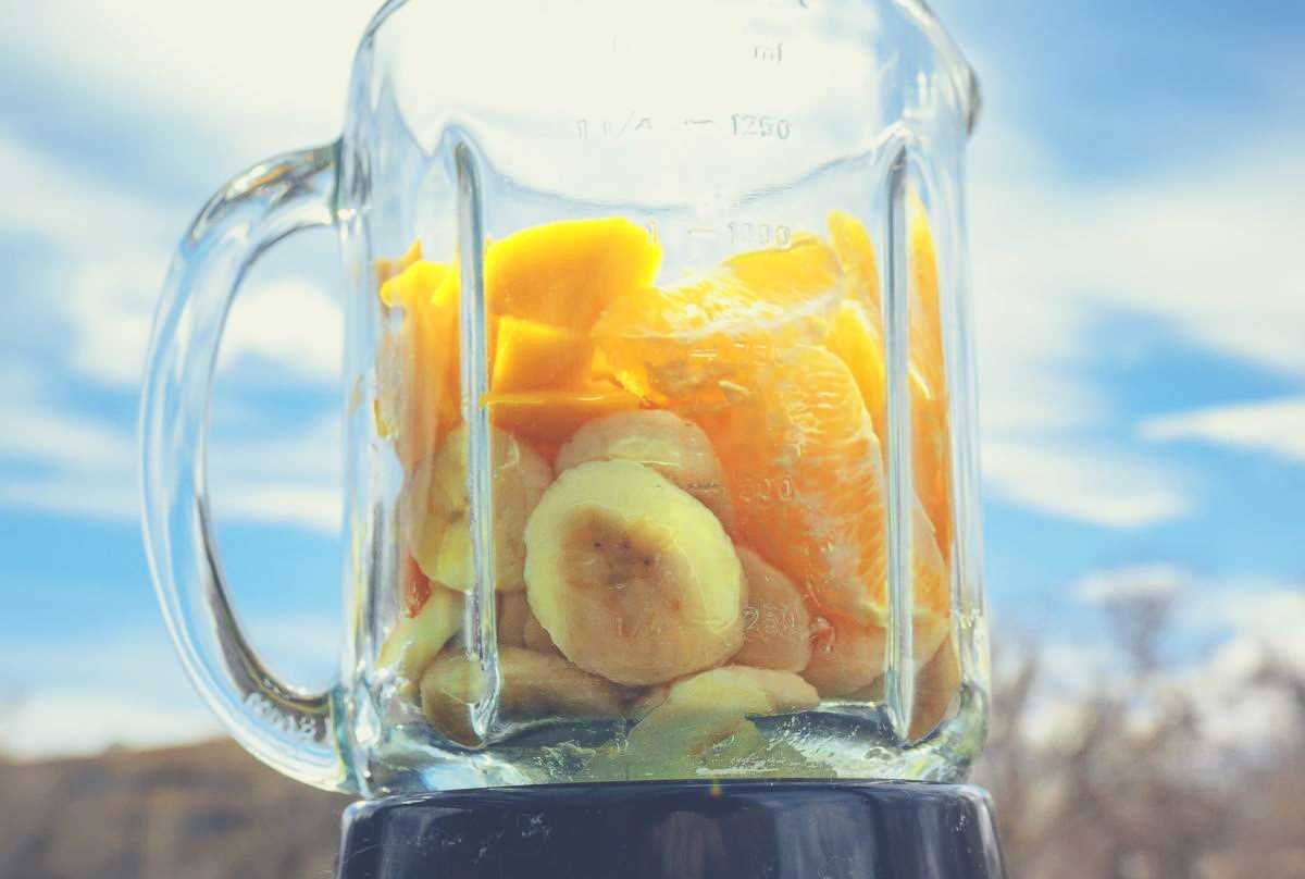 banana and pineapple in a glass blender against a cloudy blue sky