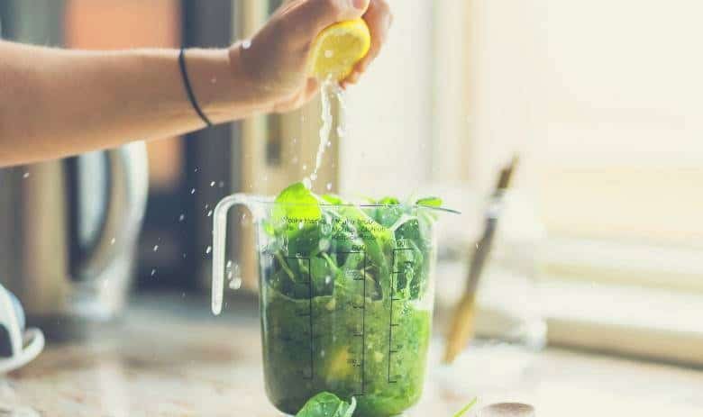 A lemon being squeezed into a blender jar while making a mojito