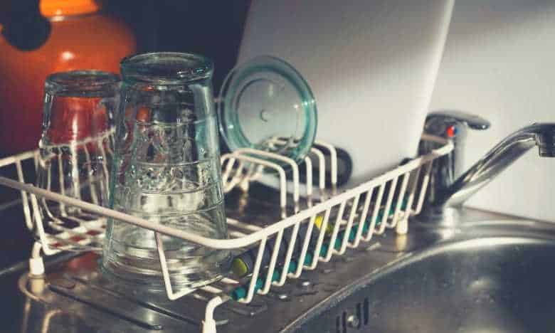A dishwashing rack on a sink, with glass on it, next to a tap