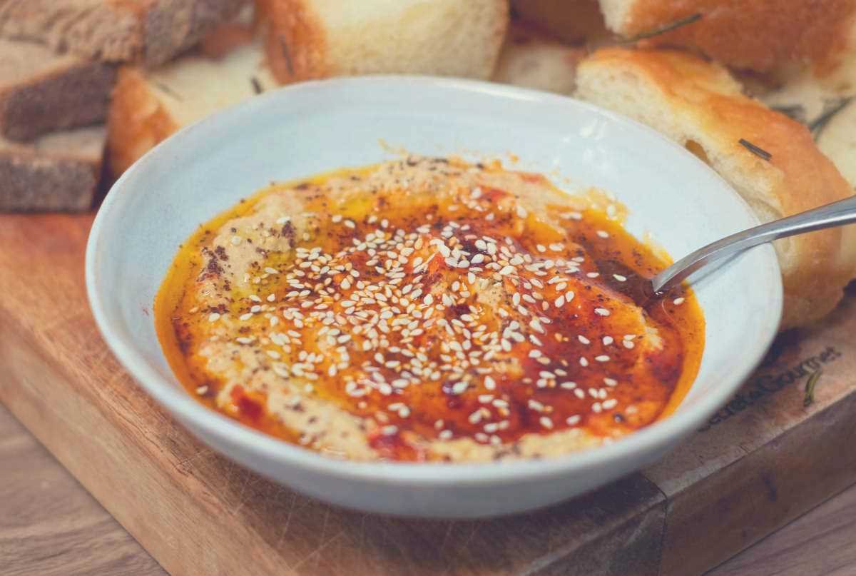 A bowl of hummus with a spoon in it, along with some crusty bread