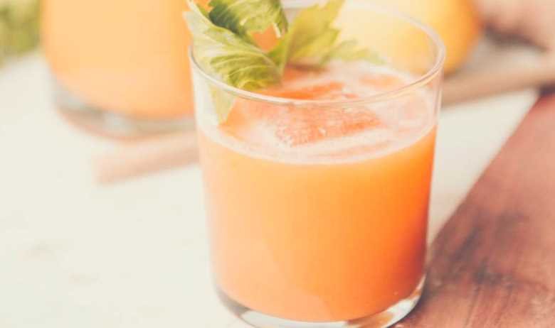a glass of carrot juice with a carrot leaf settling on the surface