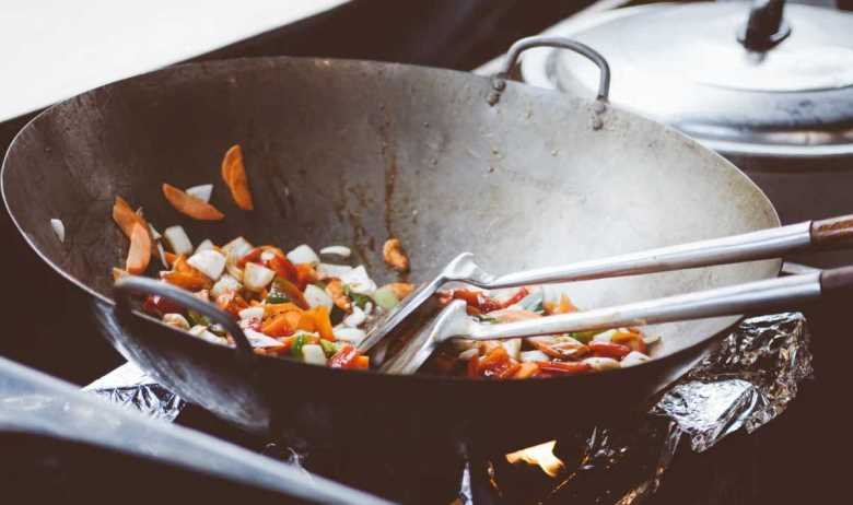 Vegetables being stir fried in a wok over a gas stovetop