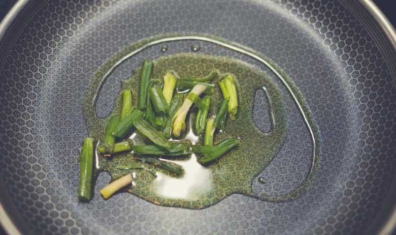 Green vegetables in oil, sitting on a non-stick cooking surface