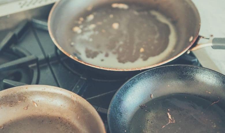 Three greasy pans sitting on the top of a cooker