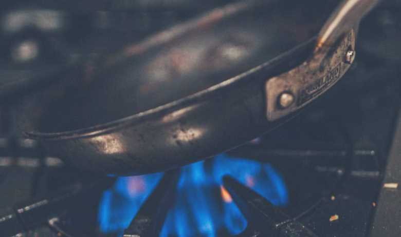 A frying pan being held close to the heat of a gas stove hob