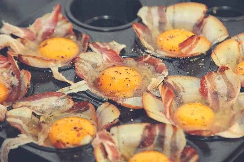 Raw eggs and bacon sitting in the cups of a muffin pan