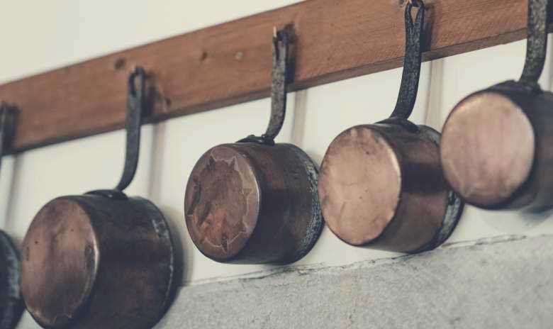 A set of copper pots and pans hanging from a wooden rack