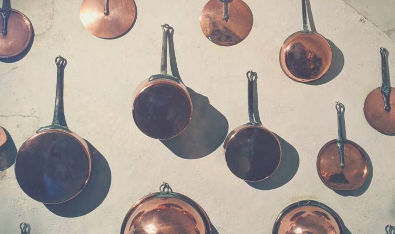 Many true copper pots and pans hanging from hooks on a kitchen wall