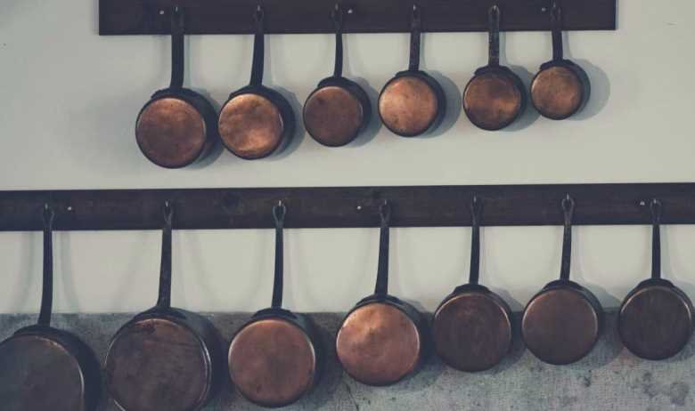 Lots of different copper pots and pans hanging from a pair of racks