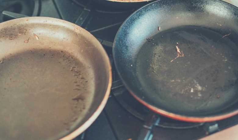 Two rusty pans, dirty from cooking, on a gas stove hob