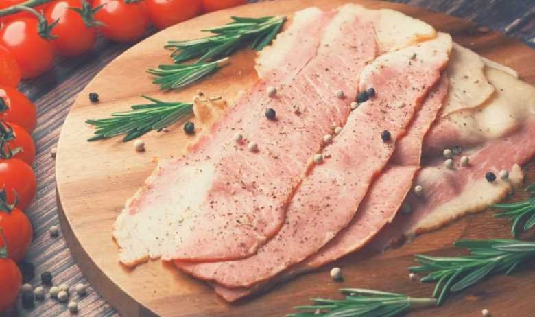 Country ham slices on a wooden platter, surrounded by rosemary and tomatoes on the vine