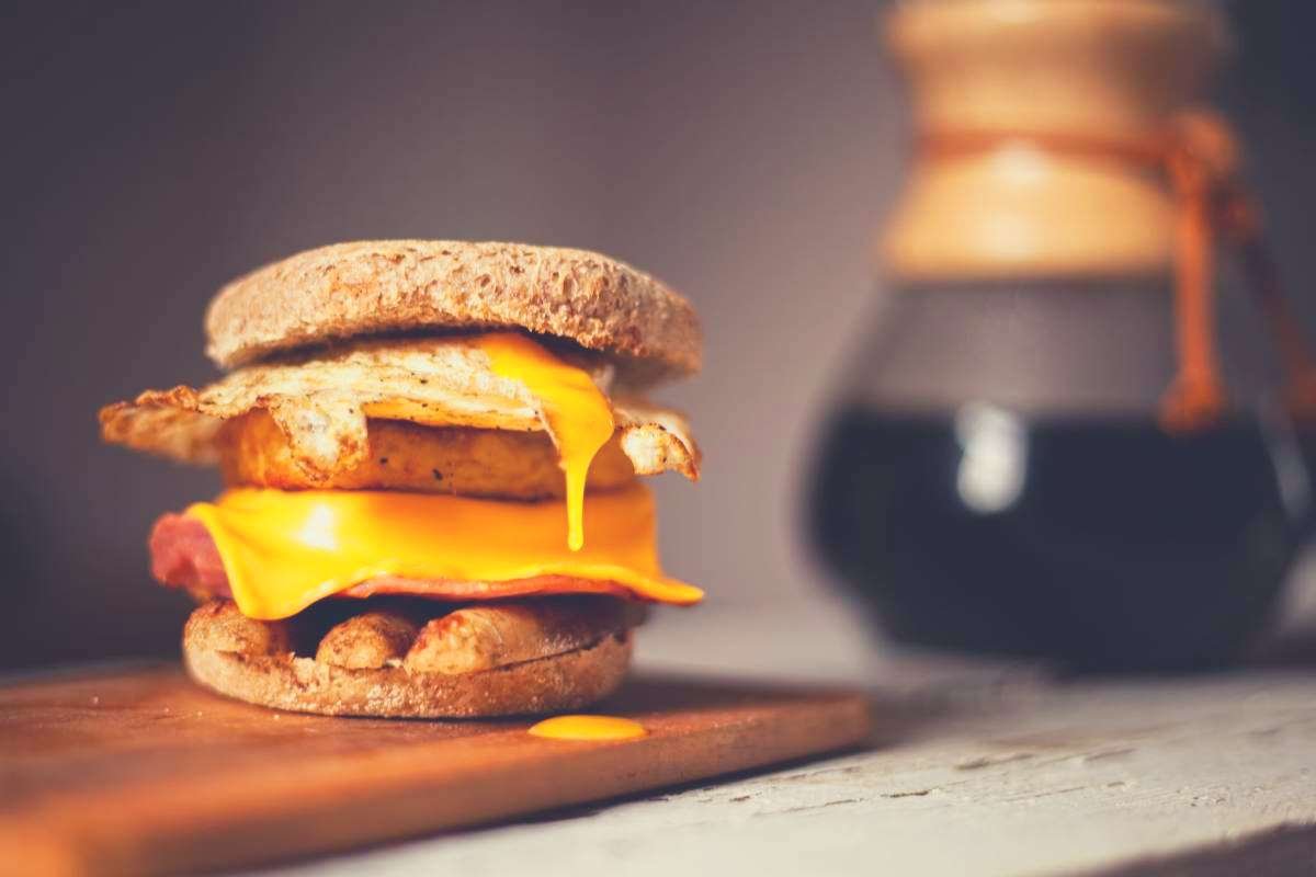 A sausage patty in a bun with egg and cheese, next to a pot of coffee