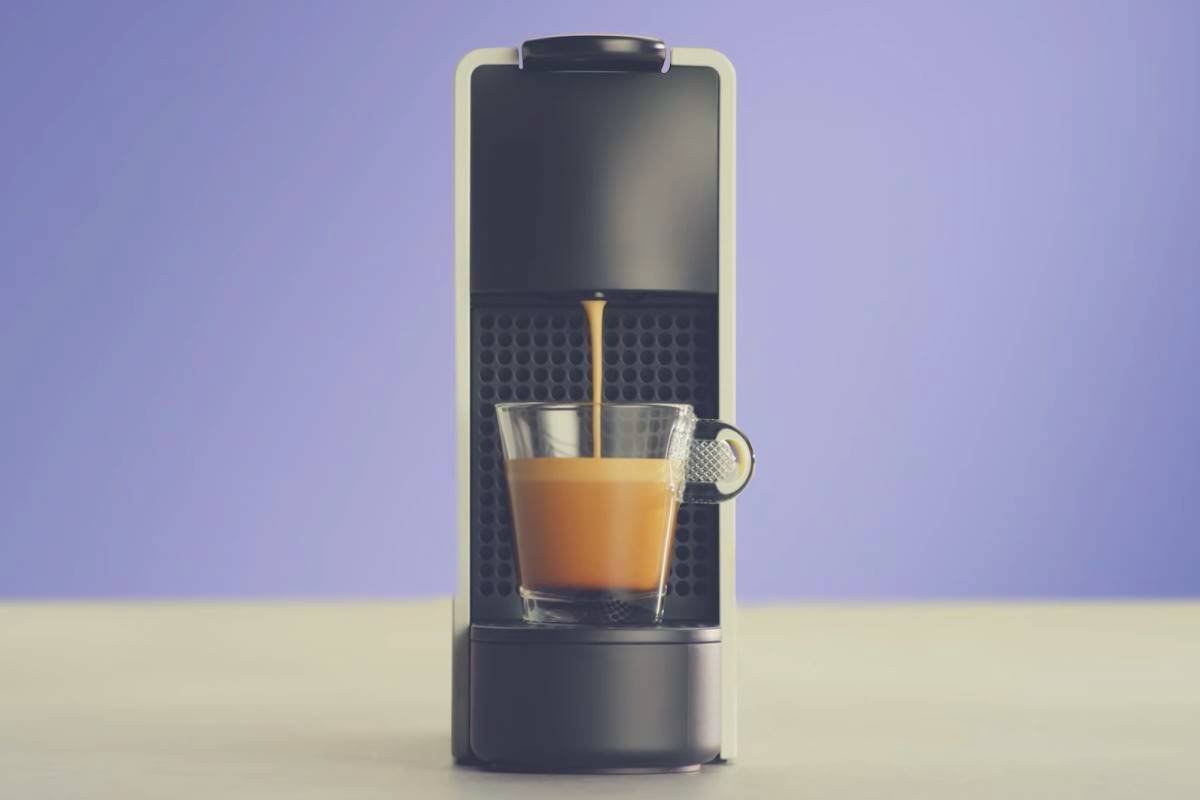 A Nespresso Essenza Mini coffee maker on a kitchen worktop against a blue background