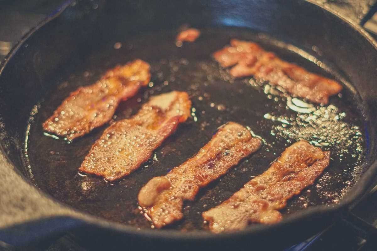 Thin cuts of bacon frying in a cast iron skillet