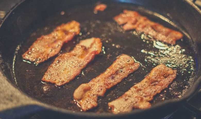 Five slices of juicy bacon sizzling in a cast iron skillet