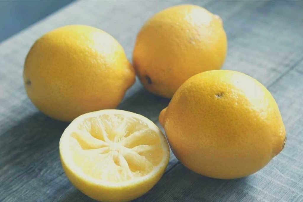 Three lemons on a cutting board, with one half of a lemon