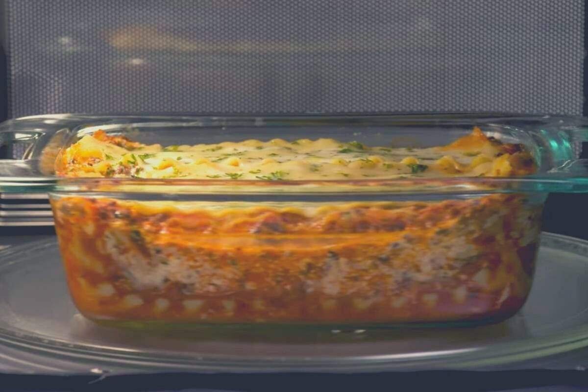 Lasagna in a clear glass dish being cooked in a microve
