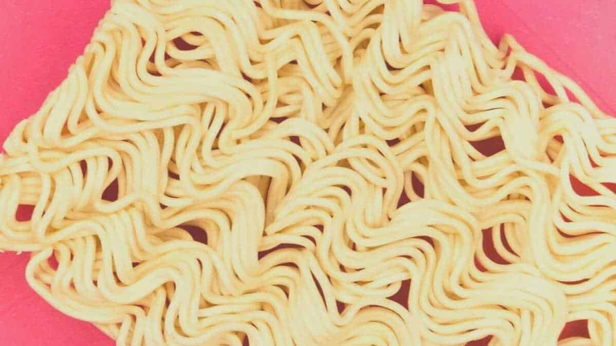 An uncooked chunk of ramen noodles on a pink background