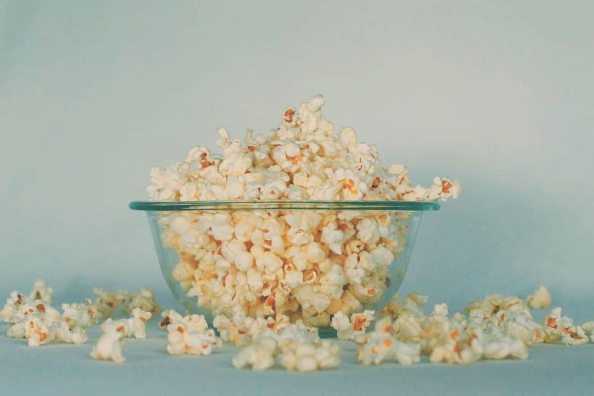 A glass bowl overfilling with popcorn, with bits of popcorn on the counter below