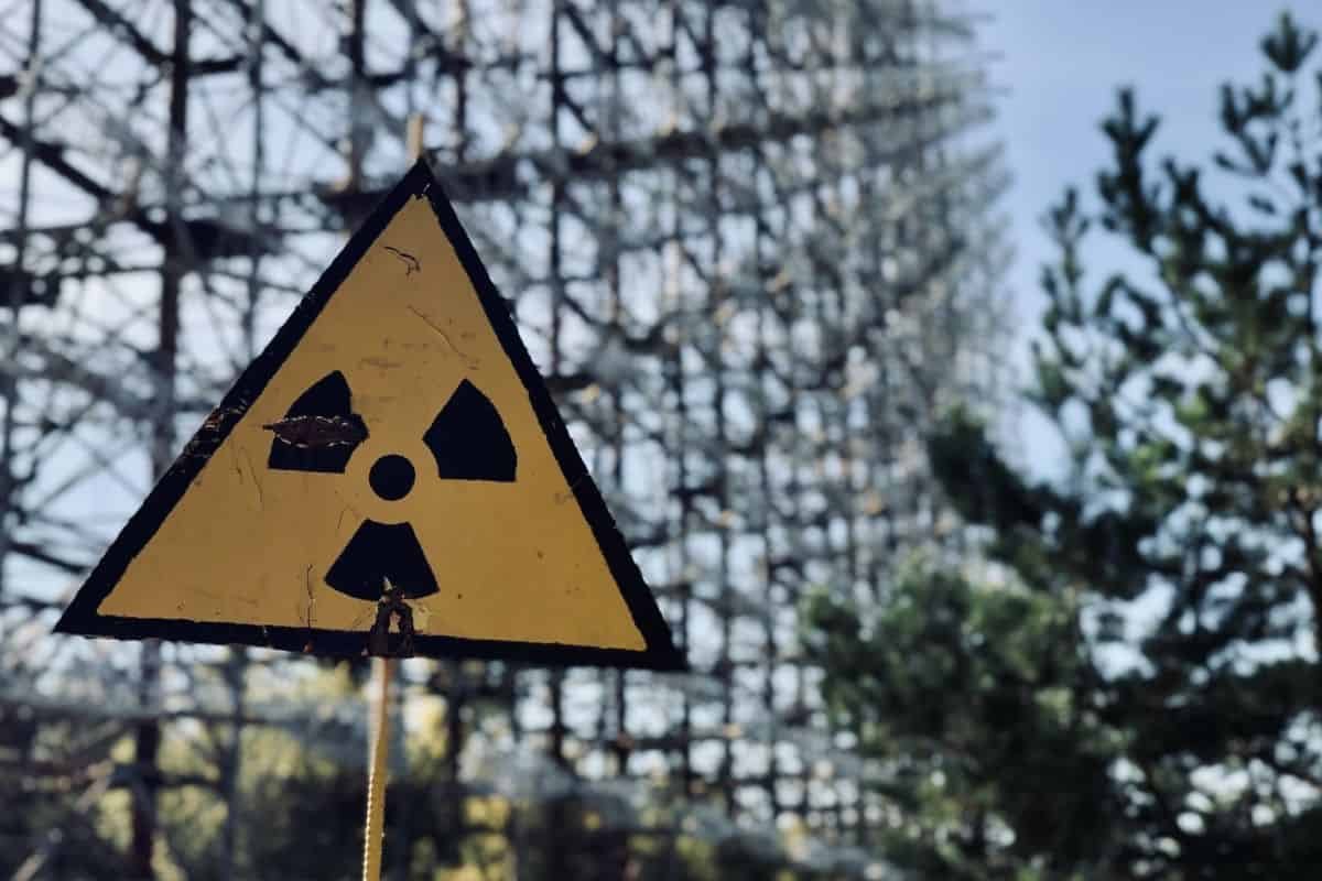 A radiation sign pinned to a chainlink fence next to trees
