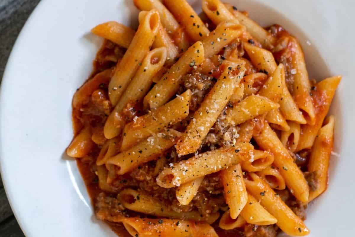 Penne pasta with a meat sauce in a white bowl.