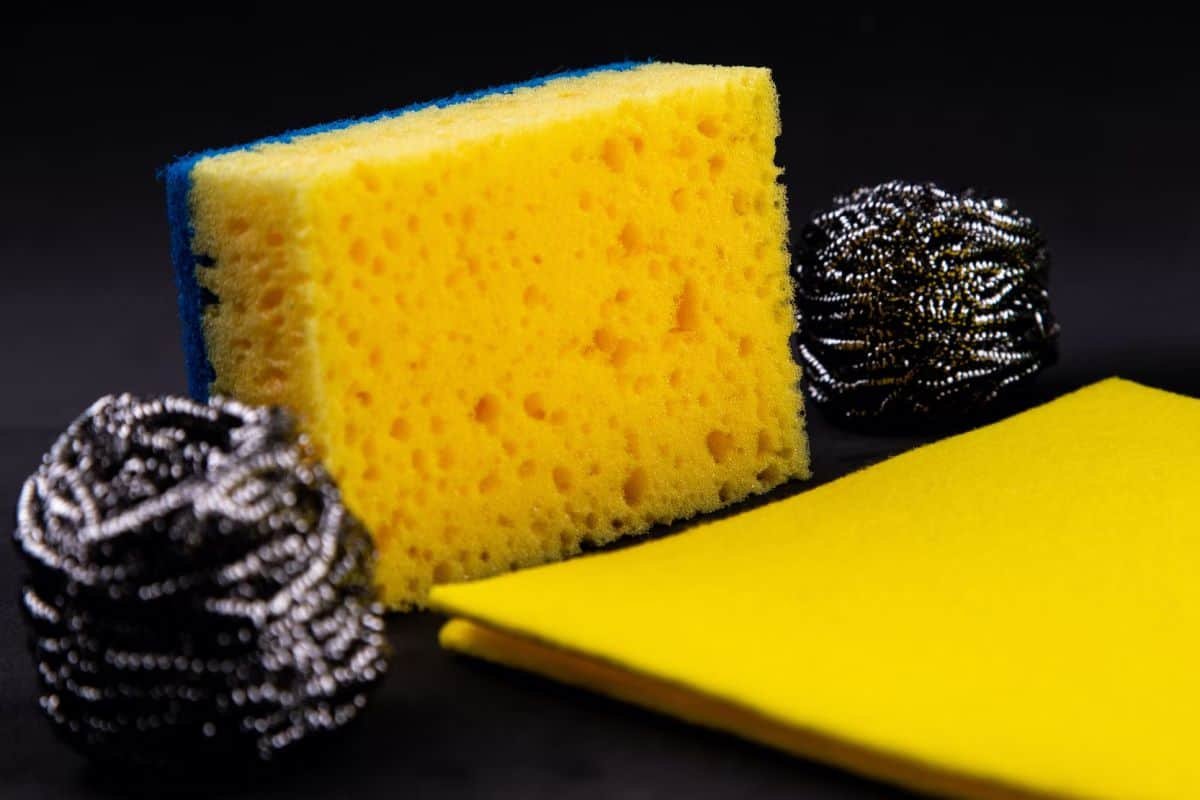 A scouring pad, yellow cleaning sponge and a cleaning cloth on a black background